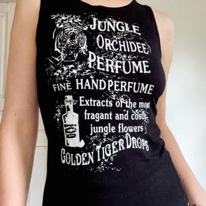 May include: Black vest top with white text reading "JUNGLE ORCHIDEE PERFUME FINE HAND PERFUME" and "GOLDEN TIGER DROPS". The top features a tiger illustration and a perfume bottle graphic. The vest top is sleeveless.