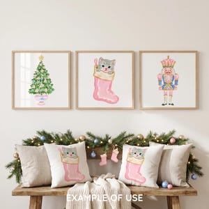 May include: Three square wall art prints featuring a watercolor Christmas tree, a gray kitten inside a pink stocking, and a pink and blue nutcracker. Below, two throw pillows display the same gray kitten in a pink stocking illustration.