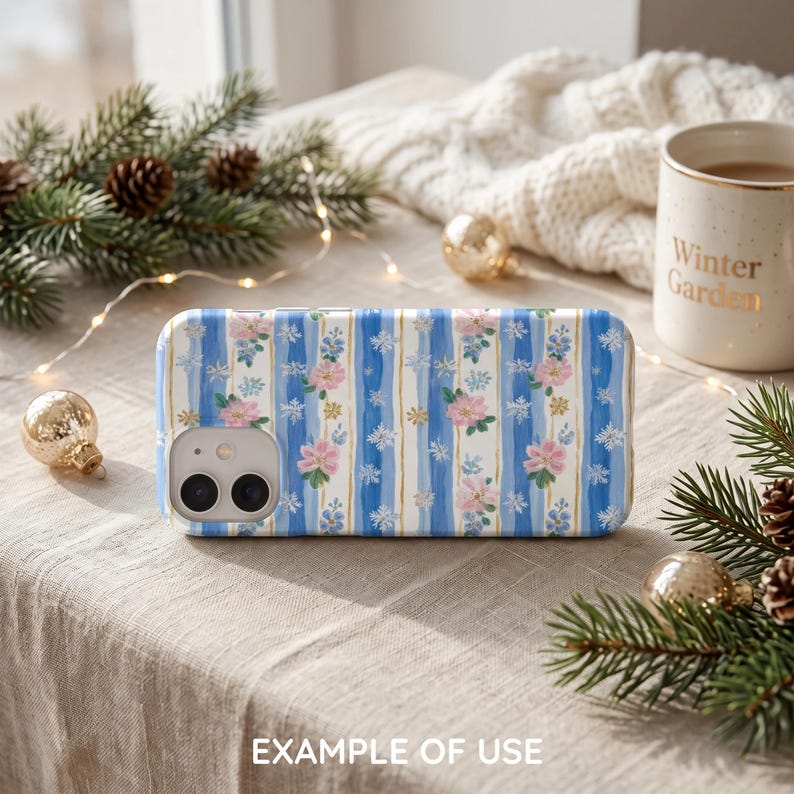 May include: A rectangular smartphone case featuring a vertical pattern of blue brushstroke stripes, pink flowers, and white snowflakes. The case has a cutout for a dual-lens camera system on the upper left corner and a smooth, glossy finish.