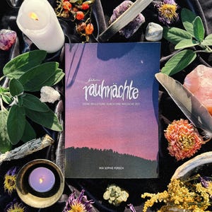 May include: A book titled "die rauch&auml;chte" with the subtitle "Deine Begleitung durch eine magische Zeit" by Mia Sophie Forsch. The book cover features a pink and purple gradient sky with a crescent moon and stars. The book is surrounded by various objects, including candles, crystals, sage, and dried flowers.