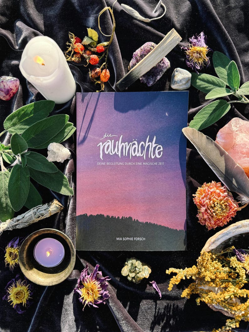 May include: A book titled "die rauch&auml;chte" with the subtitle "Deine Begleitung durch eine magische Zeit" by Mia Sophie Forsch. The book cover features a pink and purple gradient sky with a crescent moon and stars. The book is surrounded by various objects, including candles, crystals, sage, and dried flowers.
