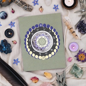 May include: A sage green rectangular book featuring a circular graphic on the cover. The graphic displays a lunar cycle, zodiac symbols, and a central flower of life pattern with the text Yule, Imbolc, Ostara, Beltane, Litha, Lughnasadh, Mabon, Samhain.