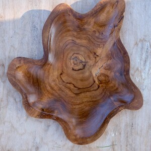 May include: A large, natural wood serving bowl with a unique, irregular shape. The bowl is made of dark brown wood with a natural grain pattern.
