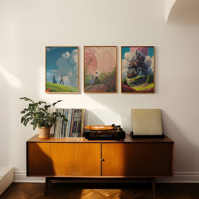 May include: Three framed prints of artwork from the animated film Howl's Moving Castle. The prints are hung on a white wall above a mid-century modern style wooden cabinet with a record player on top.