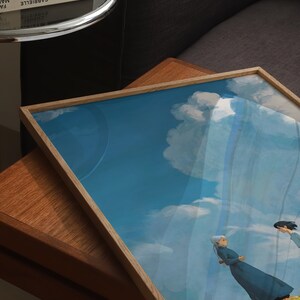 May include: A framed print of a painting depicting two figures walking on a grassy hill with a blue sky and white clouds in the background.