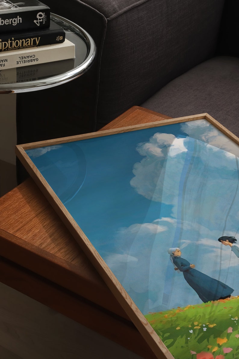 May include: A framed print of a painting depicting two figures walking on a grassy hill with a blue sky and white clouds in the background.