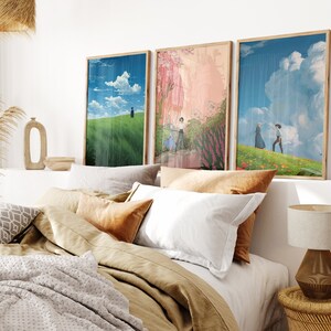 May include: Three framed art prints with a bedroom setting in the background. The prints feature a green field with a person walking, a pink and green landscape with people walking, and a blue sky with clouds and two people walking in a field.
