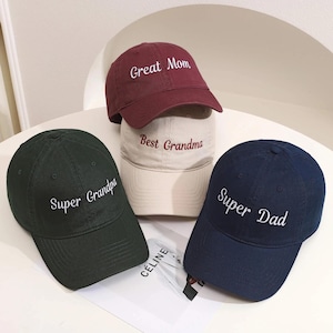 May include: Several baseball caps in shades of green, navy, and burgundy. Each cap has embroidered text: "Super Grandpa," "Great Mom," "Best Grandma," and "Super Dad." A stylish accessory.