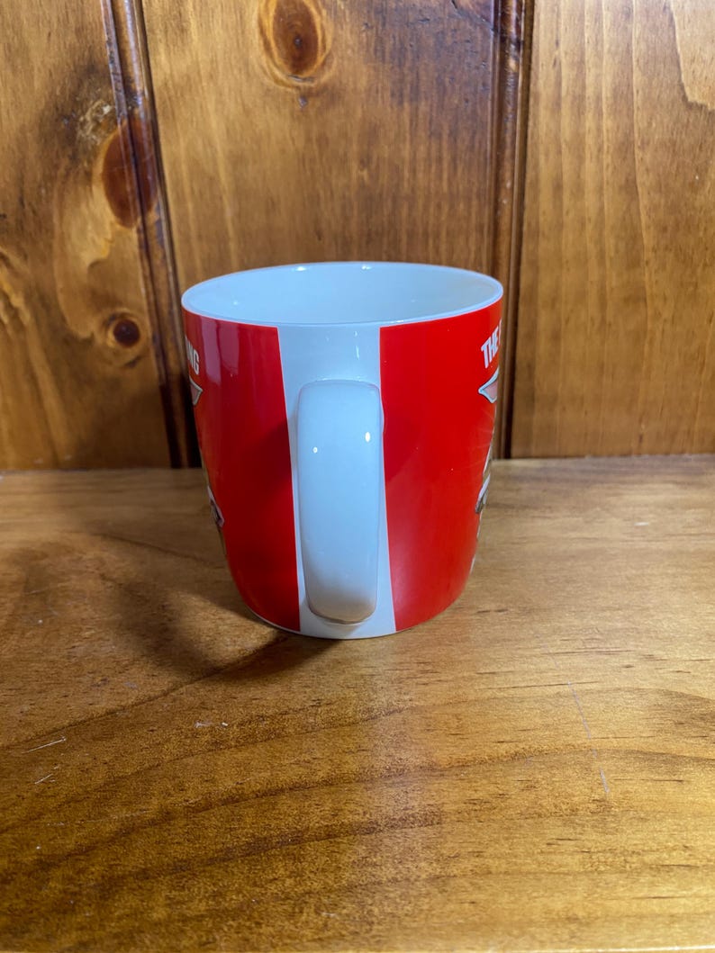 Pode incluir: Uma caneca de cer&acirc;mica branca com uma faixa exterior vermelha brilhante. A caneca tem uma pega branca curva e um interior branco. O texto vis&iacute;vel na superf&iacute;cie vermelha inclui a palavra THE em letras mai&uacute;sculas brancas, parcialmente oculta.