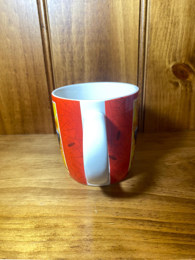 Puede incluir: Una taza de caf&eacute; de cer&aacute;mica con un asa blanca y un dise&ntilde;o a rayas rojas y blancas. La taza tiene un interior blanco y un dise&ntilde;o de telara&ntilde;a. La taza est&aacute; sobre una superficie de madera.