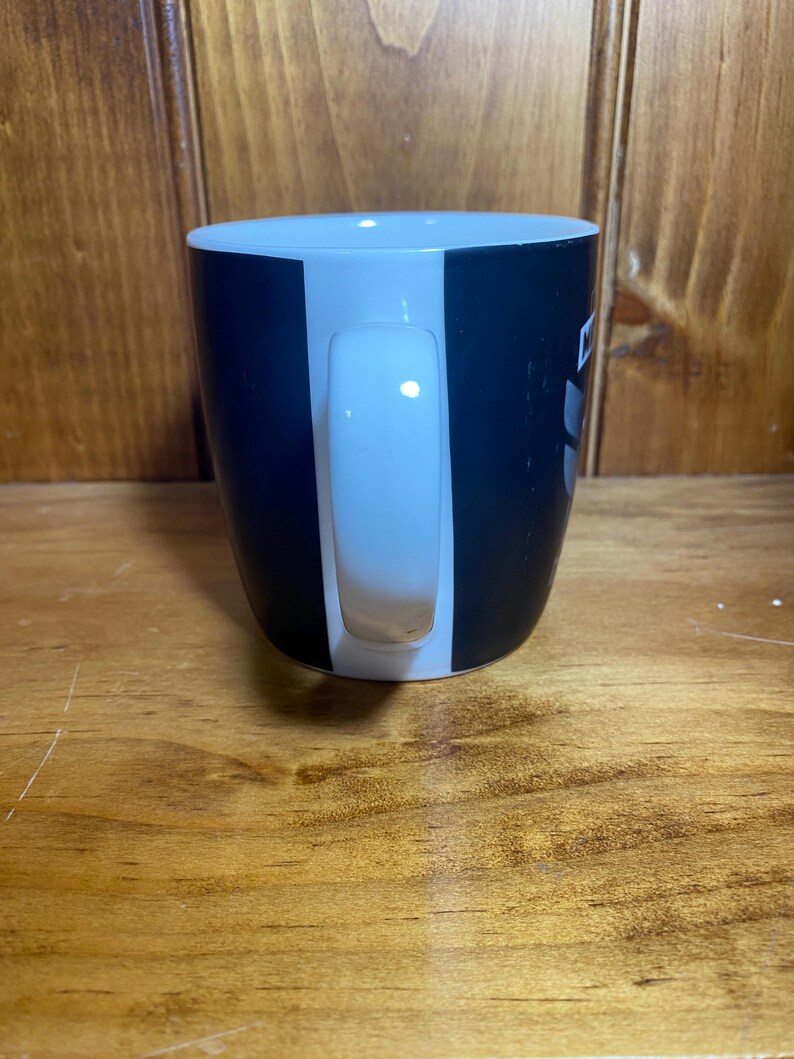 May include: A black and white ceramic coffee mug with a white handle. The mug has a vertical white stripe on the front and a black stripe on the back. The mug is sitting on a wooden surface.