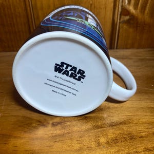 K&ouml;nnte beinhalten: Wei&szlig;e Star Wars-Keramiktasse mit einem schwarzen und blauen Design. Die Tasse tr&auml;gt das Star Wars-Logo und ist mikrowellen- und sp&uuml;lmaschinenfest.