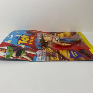 以下が含まれることがあります： ディズニーピクサーの映画トイストーリーのウッディのプラスチック製アクションフィギュアです。ウッディは、トレードマークのテンガロンハット、ベスト、ジーンズを着用しています。フィギュアは曲げることができ、ウッディとバズ・ライトイヤーの画像が描かれたカードにパッケージされています。