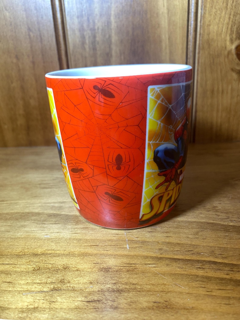 Puede incluir: Taza de cer&aacute;mica con Spider-Man. La taza tiene un fondo rojo con un patr&oacute;n de telara&ntilde;a y siluetas de ara&ntilde;as. El lado de la taza muestra a Spider-Man en acci&oacute;n. La taza es cil&iacute;ndrica con un interior blanco.