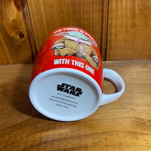 Pode incluir: Uma caneca de cer&acirc;mica vermelha com um gr&aacute;fico do Grogu e o texto THE FORCE IS STRONG WITH THIS ONE. A base exibe o log&oacute;tipo Star Wars, informa&ccedil;&otilde;es de direitos de autor e indica que a caneca pode ir ao micro-ondas e &agrave; m&aacute;quina de lavar.