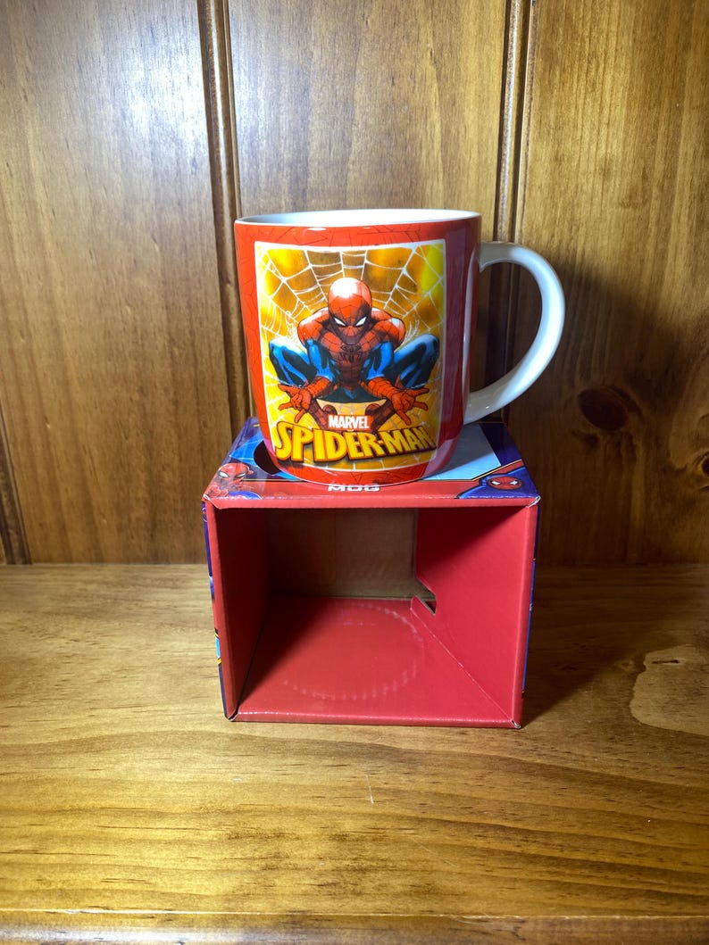 Puede incluir: Una taza de cer&aacute;mica roja con el personaje de Marvel Comics, Spider-Man. La taza tiene un asa blanca y se muestra sobre una caja roja con gr&aacute;ficos de Spider-Man. El dise&ntilde;o de la taza incluye el logotipo de Spider-Man y una imagen del superh&eacute;roe.