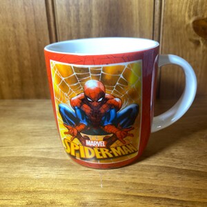 Puede incluir: Taza de cer&aacute;mica roja con Spider-Man en cuclillas sobre un fondo de telara&ntilde;a amarilla. La taza tiene un asa blanca y el logotipo de Marvel Spider-Man. Un divertido objeto de colecci&oacute;n.