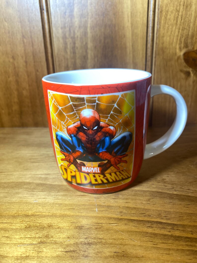 Puede incluir: Taza de cer&aacute;mica roja con Spider-Man en cuclillas sobre un fondo de telara&ntilde;a amarilla. La taza tiene un asa blanca y el logotipo de Marvel Spider-Man. Un divertido objeto de colecci&oacute;n.