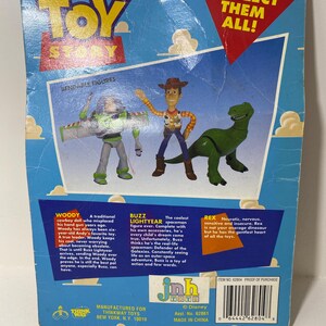 以下が含まれることがあります： トイストーリーのアクションフィギュアのパッケージ。ウッディ、バズ・ライトイヤー、レックスが描かれています。パッケージの裏面には、各キャラクターの説明が書かれています。パッケージは青、赤、緑で、「Collect Them All!」という文字が赤で書かれています。