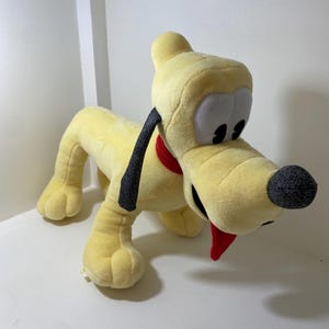 以下が含まれることがあります： 黒い耳と赤い舌を出した黄色のぬいぐるみ犬。犬は赤いリボンが付いた黒い首輪をしている。