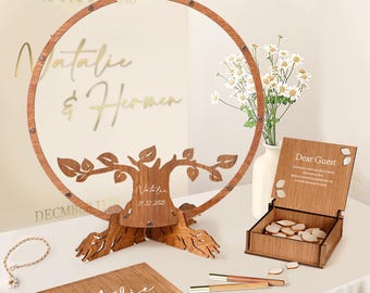 May include: A wooden wedding guest book set. The set includes a tree-shaped guest book, a box with wooden hearts, a guest book, and pens. The tree has the names "Natalie & Hermen" and the date "December 11, 2025".