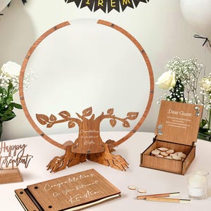 May include: Wooden retirement guest book set. Includes a tree-shaped guest book with a round frame, a wooden box with guest tokens, and a guest book. The tree frame has the text "Congratulations on Your Retirement! Kristin".
