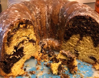 May include: A marble cake with a white glaze, partially sliced and showing the inside of the cake. The cake is on a blue and white plate.