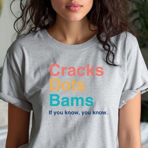 May include: Gray t-shirt with the text "Cracks Dots Bams" in colorful letters. The text is followed by the phrase "If you know, you know."
