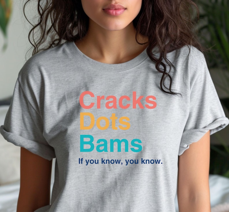 May include: Gray t-shirt with the text "Cracks Dots Bams" in colorful letters. The text is followed by the phrase "If you know, you know."