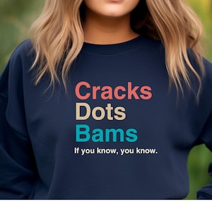 May include: A navy blue sweatshirt with the text "Cracks Dots Bams" in colorful letters. The text is followed by the phrase "If you know, you know."