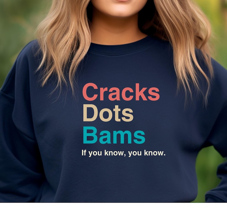 May include: A navy blue sweatshirt with the text "Cracks Dots Bams" in colorful letters. The text is followed by the phrase "If you know, you know."