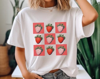 May include: White t-shirt with a red and white checkered pattern featuring a repeated image of a strawberry.
