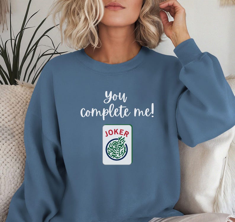 Puede incluir: Una sudadera azul con el texto "you complete me!" y un gr&aacute;fico de carta de joker verde y blanco.