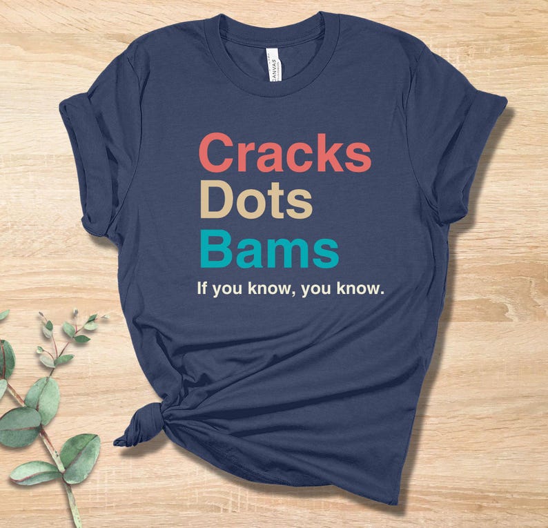 May include: A navy blue t-shirt with the text "Cracks Dots Bams" in colorful letters. The text is followed by the phrase "If you know, you know."