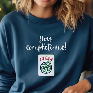 Puede incluir: Una sudadera azul marino con el texto "You complete me!" y un gr&aacute;fico de una carta de joker.