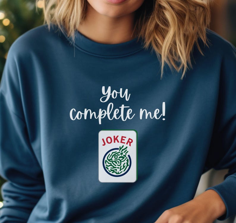 Puede incluir: Una sudadera azul marino con el texto "You complete me!" y un gr&aacute;fico de una carta de joker.