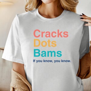 May include: White t-shirt with the text "Cracks Dots Bams" in colorful letters and the phrase "If you know, you know." printed below.