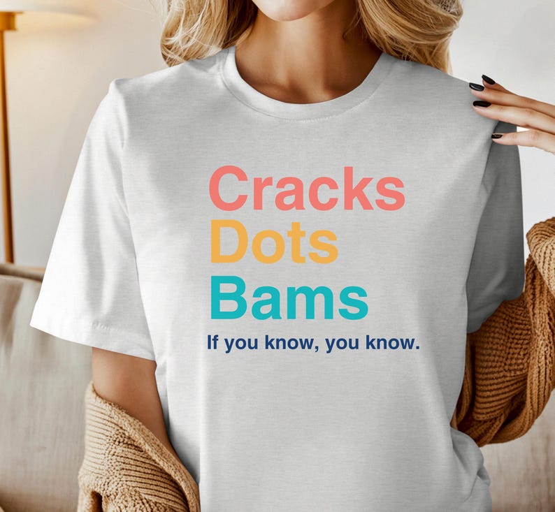 May include: White t-shirt with the text "Cracks Dots Bams" in colorful letters and the phrase "If you know, you know." printed below.