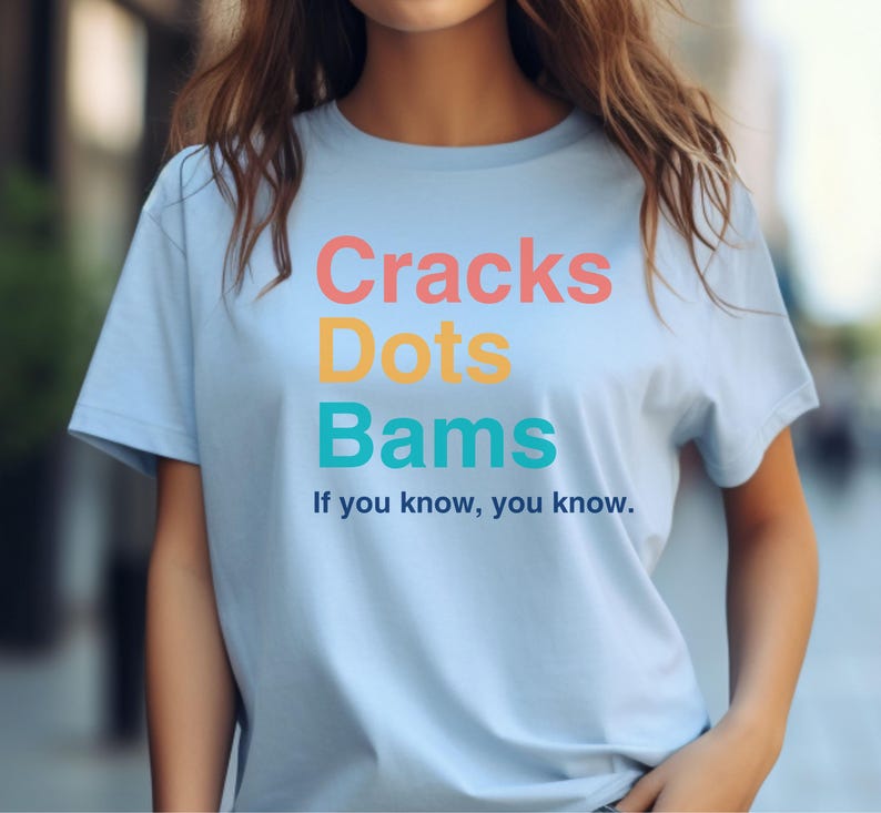 May include: A light blue t-shirt with the text "Cracks Dots Bams" in colorful letters. The text "If you know, you know." is printed below the colorful text.