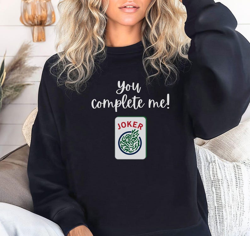 Puede incluir: Sudadera negra con el texto "you complete me!" y un gr&aacute;fico de carta de joker verde y blanco.