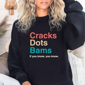 May include: Black sweatshirt with the text "Cracks Dots Bams" in colorful letters and the phrase "If you know, you know."