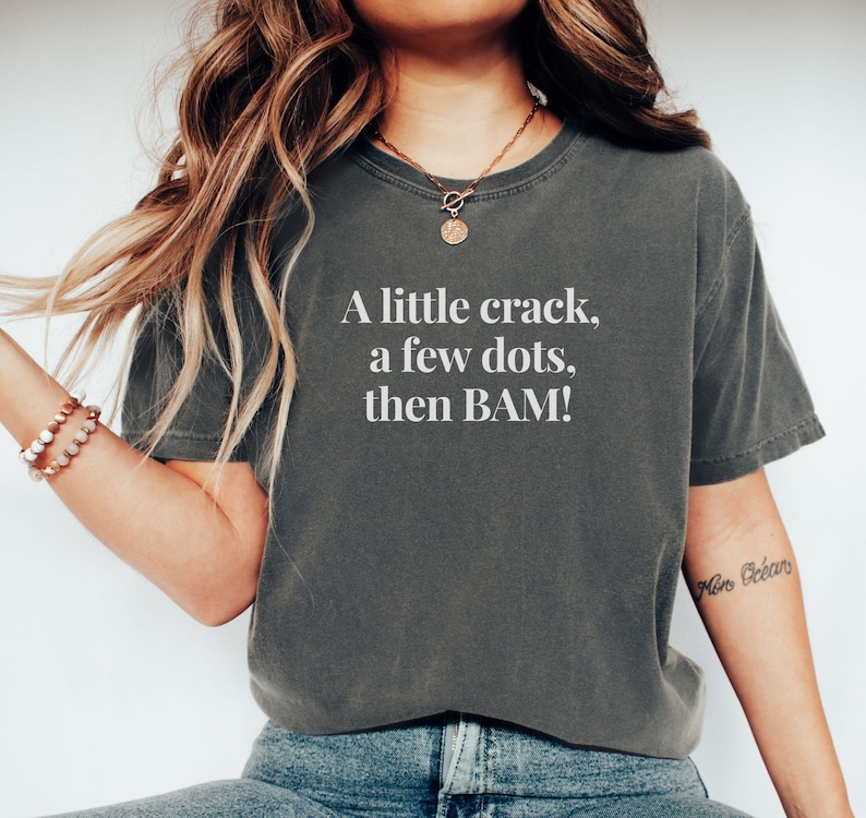 May include: Dark gray t-shirt with the text "A little crack, a few dots, then BAM!" in white. The shirt is a comfortable, casual style.