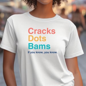 May include: White t-shirt with the text "Cracks Dots Bams" in rainbow colors and the phrase "If you know, you know." in blue.