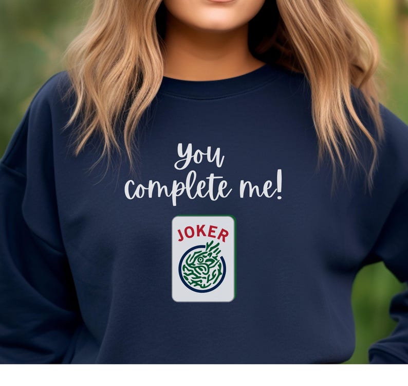 Puede incluir: Una sudadera azul marino con el texto "You complete me!" y un gr&aacute;fico de una carta de joker con un dise&ntilde;o verde y blanco.