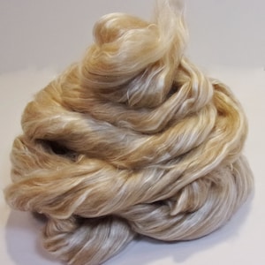 May include: A pile of light brown and white silk fibers. The fibers are soft and fluffy, and they are perfect for spinning or felting.