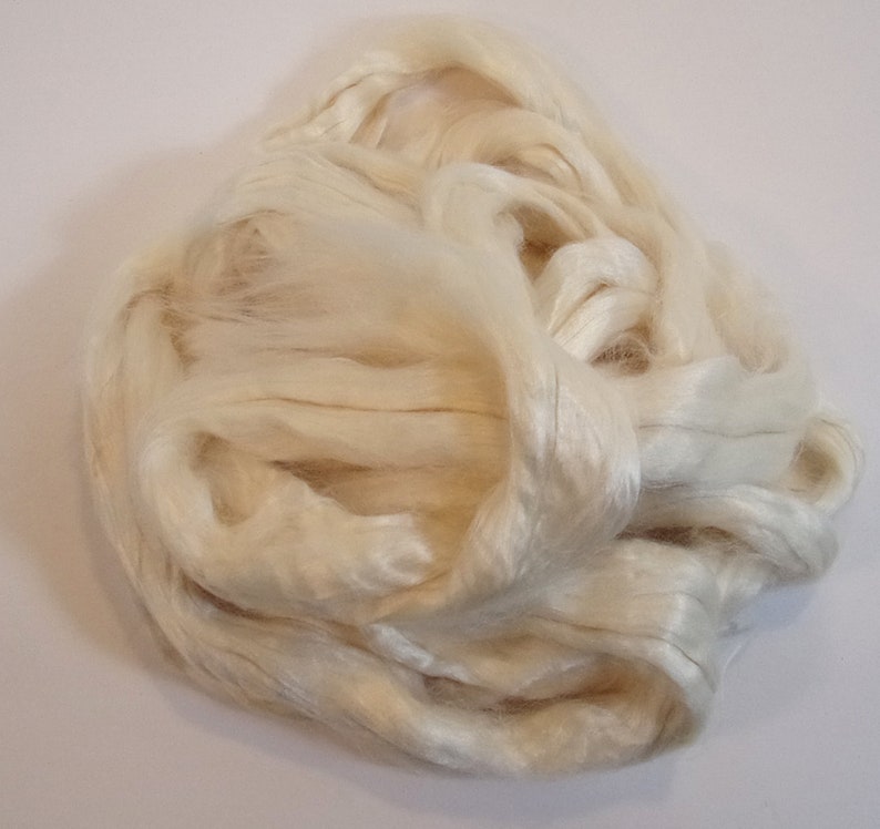 May include: A close-up of a pile of white silk fibers. The fibers are soft and fluffy, and they are perfect for spinning or weaving.