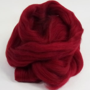 May include: A close-up of a mass of deep red wool roving. The fibers are soft and fluffy, with a slightly textured appearance. The wool is tightly packed and appears to be ready for felting or other fiber crafts.