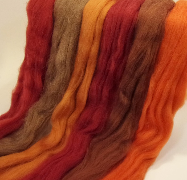 May include: A collection of six strands of wool yarn in shades of orange, red, and brown. The yarn is arranged in a gradient from light orange to dark brown.