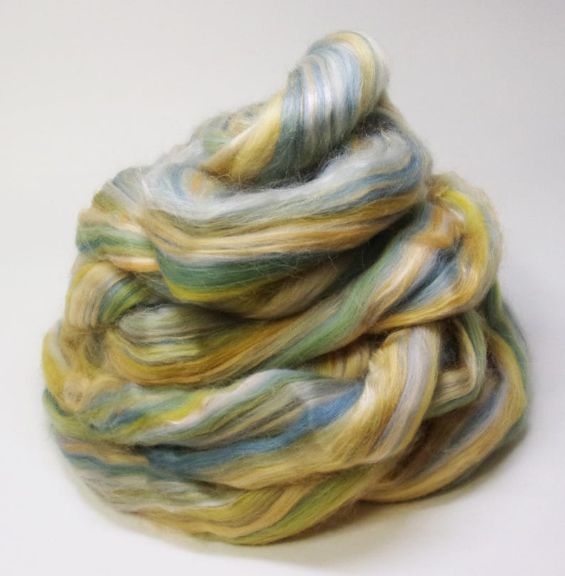 May include: A pile of colorful fiber for spinning, featuring shades of yellow, green, blue, and white. The fiber is soft and fluffy, ideal for creating yarn for knitting or other fiber arts projects.