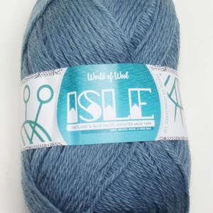 May include: A skein of blue yarn labeled "World of Wool Isle Shetland & Blue Faced Leicester Aran Yarn 100% British Wool 100g Ball Made in Yorkshire, UK"